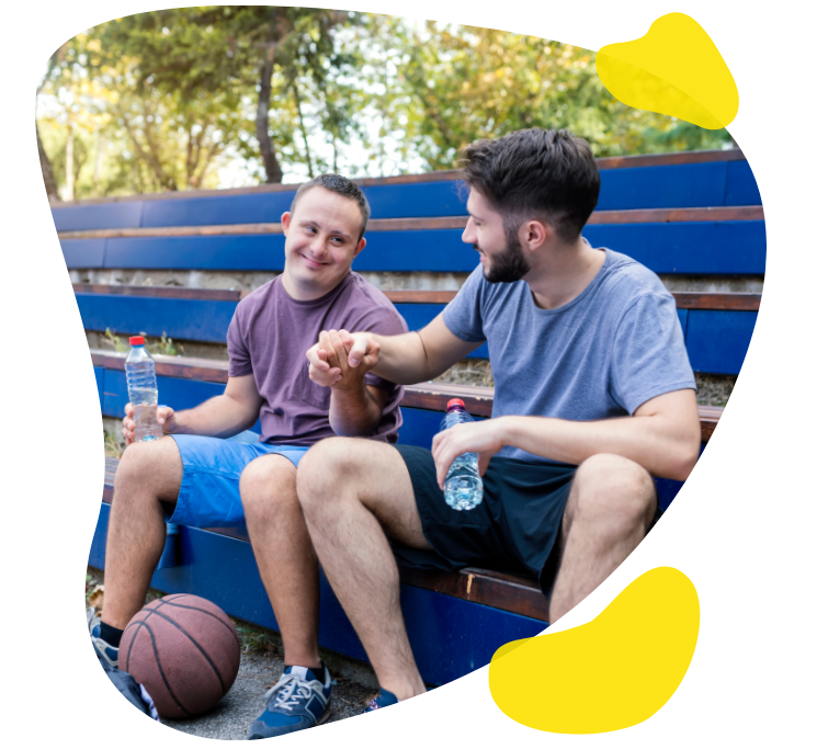 Two people sit on a park bench smiling and shaking hands after a game of basketball.