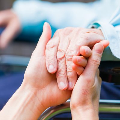This is an image of two people holding hands. One person is in a wheelchair.