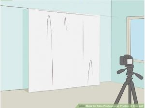 A camera on a tripod is positioned in front of a white sheet hanging from the wall. 