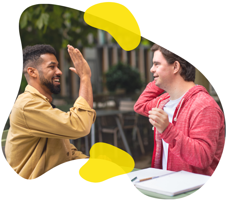 Two young men high five over coffee in a leafy green outdoor cafe